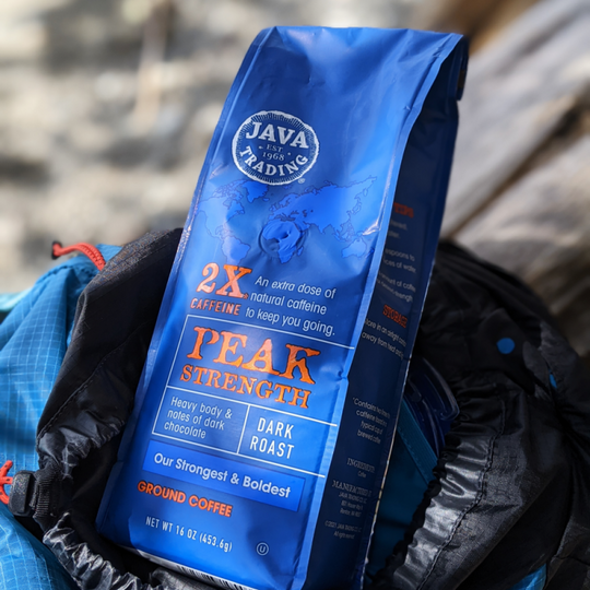 Bag of Java Trading Peak Strenght High Caffeine 16 ounces ground coffee, sitting top of a blue backpack.