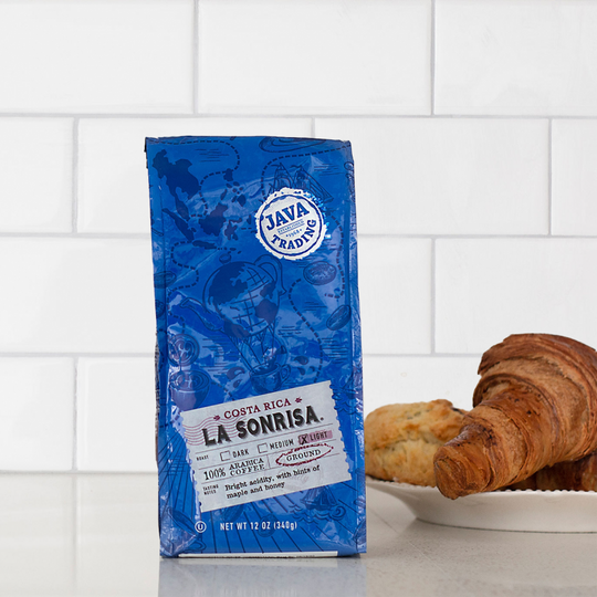 Bag of 12 ounce Costa Rica La Sonrisa coffee on a kitchen counter with a plate of croissants