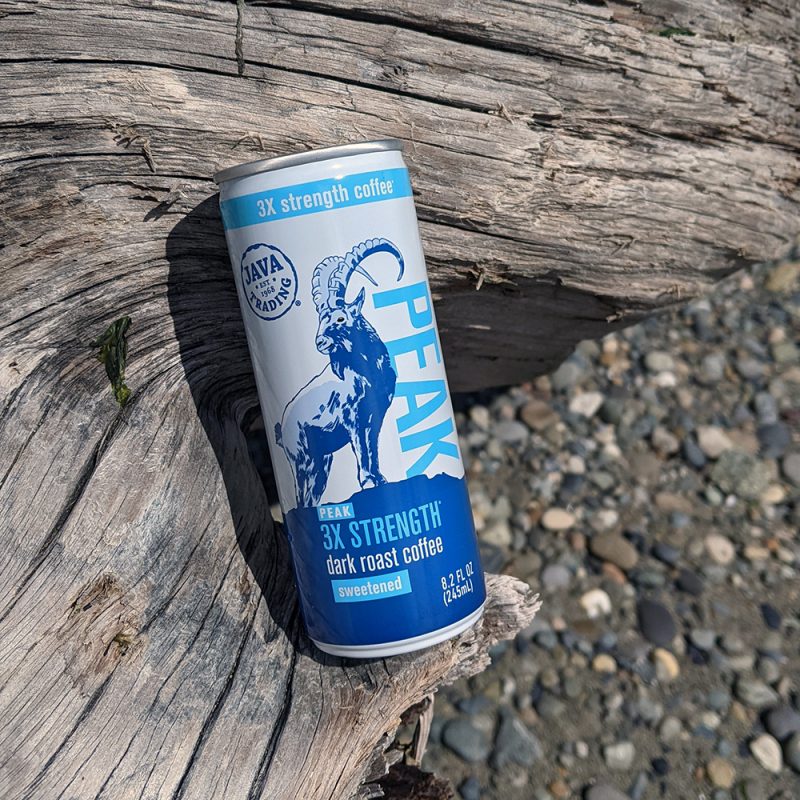 Can of Java Trading Peak High Caffeine can resting on a log on a beach