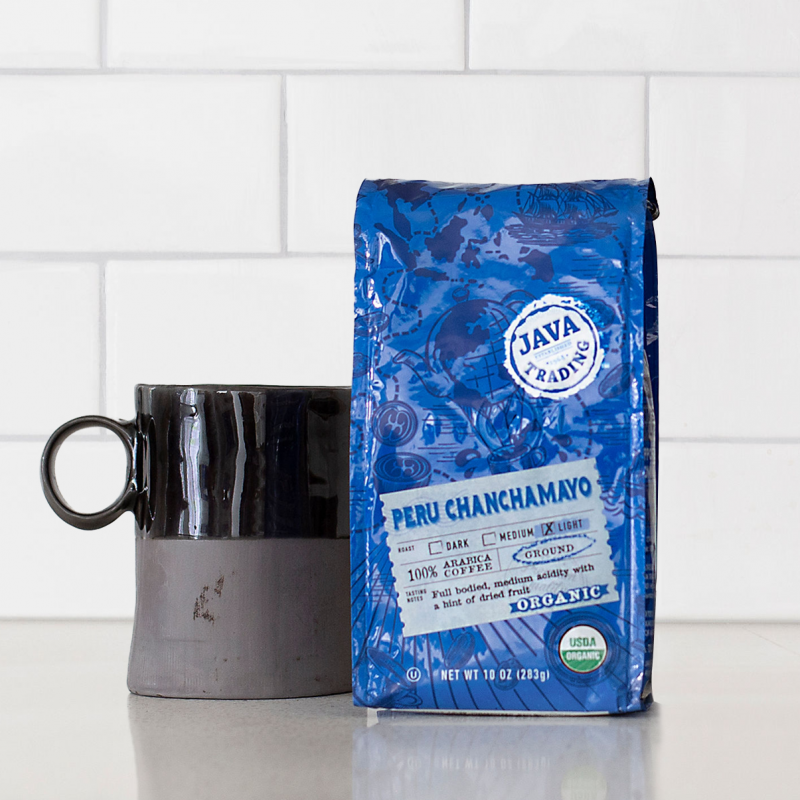 Bag of 10 ounce Organic Peru Chanchamayo on a kitchen counter with mug